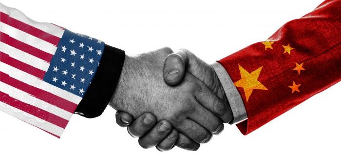 Two business men shaking hands with one mans sleeve painted in an American flag and the other mans sleeve painted in a China Flag